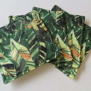 May include: Set of four green and yellow fabric coasters with a tropical leaf pattern. The coasters are square and have a stitched edge.