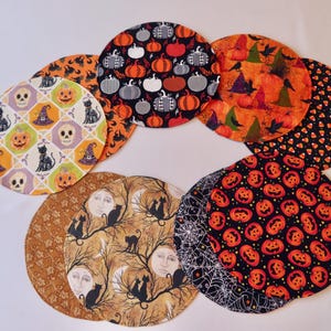 May include: Set of eight Halloween-themed placemats featuring various designs including pumpkins, cats, witches, skulls, and candy corn. The placemats are made of fabric and have a round shape.