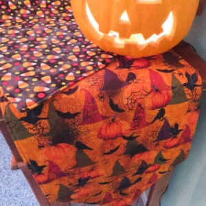 May include: Halloween table runner with a black and orange candy corn pattern on one side and a black and orange witch hat and pumpkin pattern on the other side.