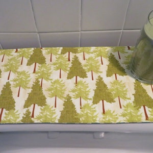 May include: A green and white toilet tank lid cover with a pattern of green trees. A clear glass jar candle with a green wax is sitting on the cover.