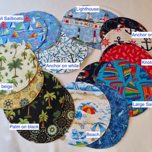 May include: Ten round fabric placemats with various nautical themes.  The placemats feature designs such as palm trees, sailboats, anchors, knots, and lighthouses.  The placemats are in various colors, including blue, red, white, beige, and black.