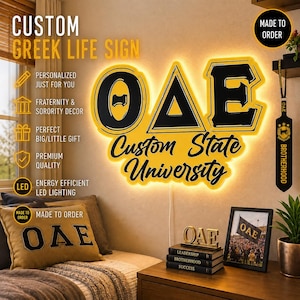 May include: A custom Greek life sign with the letters OAE in black and yellow, illuminated with LED lighting. The sign is personalized and features the words "Custom State University." Other items include a pillow, framed photo, and books with the letters OAE.