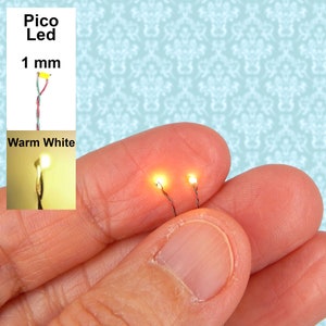 May include: Two warm white 1 mm pico LEDs with thin wires, lit and held in a hand against a blue and white patterned background. The text "Pico Led 1 mm Warm White" is visible in the image.