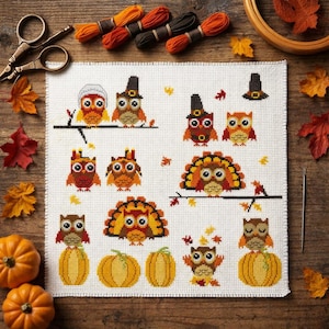 Op de afbeelding: Een wit stoffen vierkant met een kruissteekpatroon van diverse uilen, kalkoenen en pompoenen in herfstkleuren. Het ontwerp bevat uilen met hoeden, kalkoenen met gespreide veren en pompoenen, gerangschikt op een raster met verspreide bladeren.