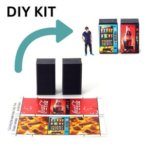 May include: DIY kit for miniature vending machines. The kit includes two black rectangular blocks, a printed sheet with Coca-Cola and snack designs, and a teal arrow. Two assembled vending machines and a miniature figure are also shown.