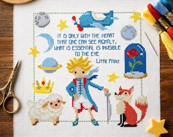 May include: A cross-stitch pattern on white fabric featuring the Little Prince, a sheep, a fox, a rose in a glass dome, a plane, and planets. The text reads: It is only with the heart that one can see rightly, what is essential is invisible to the eye.