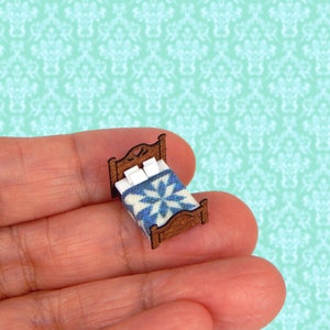 May include: A miniature wooden bed with a blue and white patterned quilt and white pillows. The bed is made of wood and has a simple design.