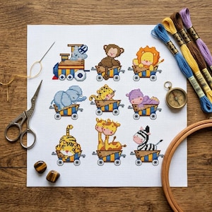 May include: A white Aida fabric featuring a cross-stitch pattern of nine colorful animals in small train cars, including a monkey, lion, elephant, and zebra. The kit includes embroidery floss in blue, yellow, brown, and purple, scissors, and a hoop.