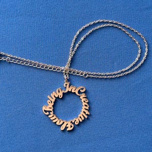 May include: A silver necklace with a circular pendant that reads "Being Creative" in a cursive font.