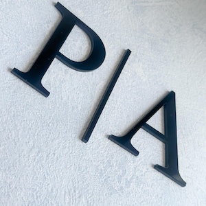 May include: Black acrylic letters spelling "P/A" mounted on a white textured wall.