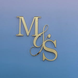 May include: Gold-coloured metal initials "M" and "S" in a decorative script font. The letters are placed against a gradient background of blue and purple.