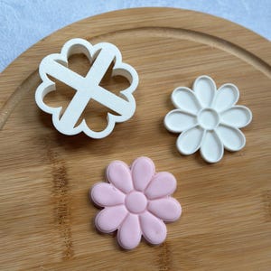 Pode incluir: Tr&ecirc;s cortadores de biscoitos em forma de flores. Dois s&atilde;o brancos e um &eacute; rosa.