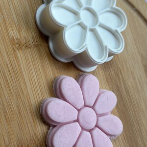 Pode incluir: Dois cortadores de biscoitos em forma de flor, um branco e outro rosa. O cortador branco est&aacute; em cima do cortador rosa.