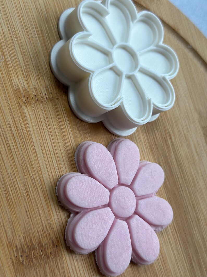 Pode incluir: Dois cortadores de biscoitos em forma de flor, um branco e outro rosa. O cortador branco est&aacute; em cima do cortador rosa.