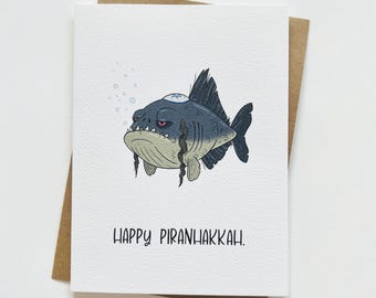 May include: A greeting card featuring a cartoon illustration of a fish wearing a yarmulke. The text on the card reads "Happy Piranhakkah."