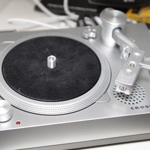 May include: Silver Crosley RSD3 turntable with a black record and silver arm. The turntable has a volume knob and a red power indicator light. The brand name and model are printed on the front.