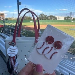 May include: White tote bag with red handles and a baseball-themed tag that says "Carter #1". Baseball earrings with red glitter tops and white baseball-shaped bottoms with red stitching are also visible.