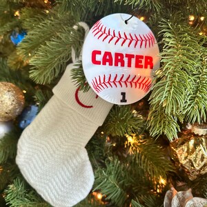 Pu&ograve; includere: Calza bianca a maglia con ricamo rosso appesa a un albero di Natale verde con un ornamento da baseball bianco con cuciture rosse e il nome "CARTER" e il numero "1" su di esso.