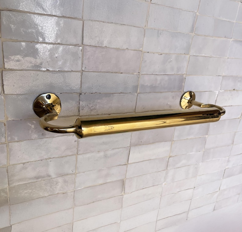 Peut inclure: Un porte-serviettes dor&eacute; avec un design incurv&eacute;, mont&eacute; sur un mur carrel&eacute; blanc. La barre a une section centrale cylindrique et des plaques de montage circulaires. Le design g&eacute;n&eacute;ral est simple et &eacute;l&eacute;gant.
