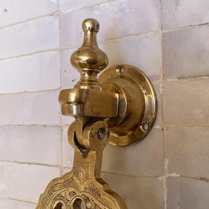 Puede incluir: Un aldaba de puerta de lat&oacute;n dorado con un dise&ntilde;o ornamentado. La aldaba est&aacute; montada sobre una placa redonda con agujeros para tornillos. Tiene un mango decorativo y una secci&oacute;n inferior detallada y estampada. El acabado es dorado brillante.