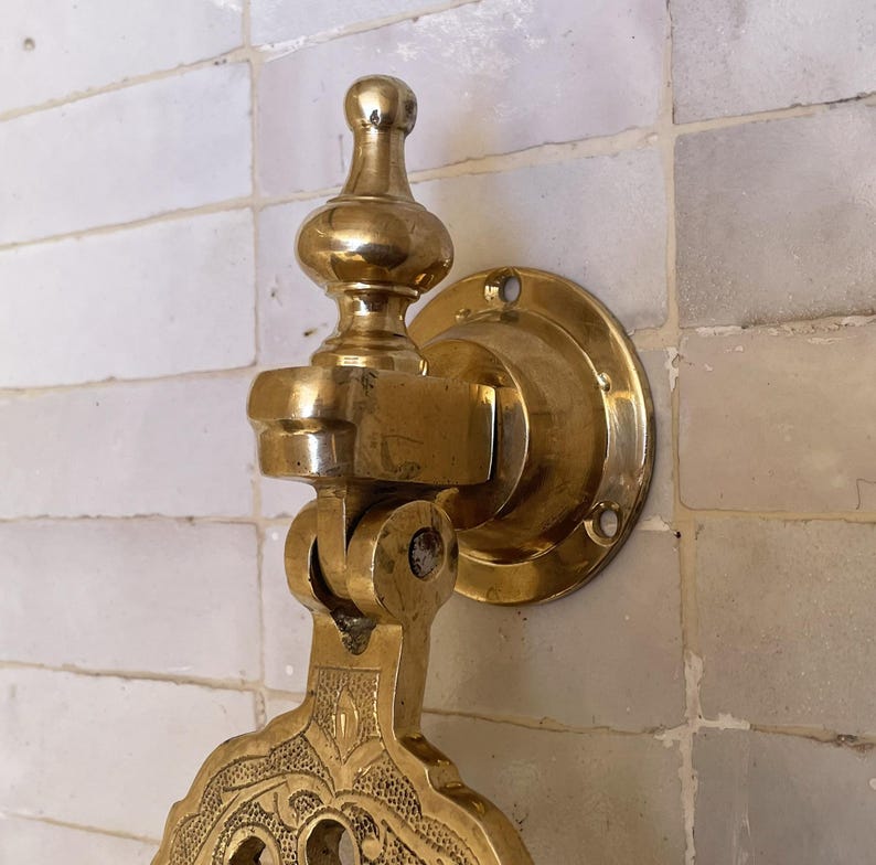 Puede incluir: Un aldaba de puerta de lat&oacute;n dorado con un dise&ntilde;o ornamentado. La aldaba est&aacute; montada sobre una placa redonda con agujeros para tornillos. Tiene un mango decorativo y una secci&oacute;n inferior detallada y estampada. El acabado es dorado brillante.