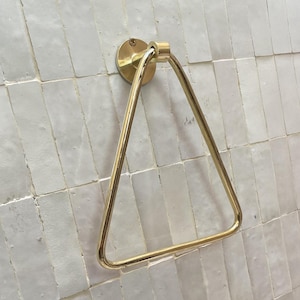 Triangle-shaped brass towel ring mounted on white zellige tiles