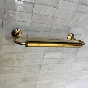Peut inclure: Un porte-serviettes dor&eacute; avec une section centrale cylindrique et des extr&eacute;mit&eacute;s incurv&eacute;es. La barre est fix&eacute;e sur un mur carrel&eacute; de couleur claire. Le design est simple et &eacute;l&eacute;gant, adapt&eacute; &agrave; une salle de bain ou une cuisine. Mesure environ 40 cm de long.