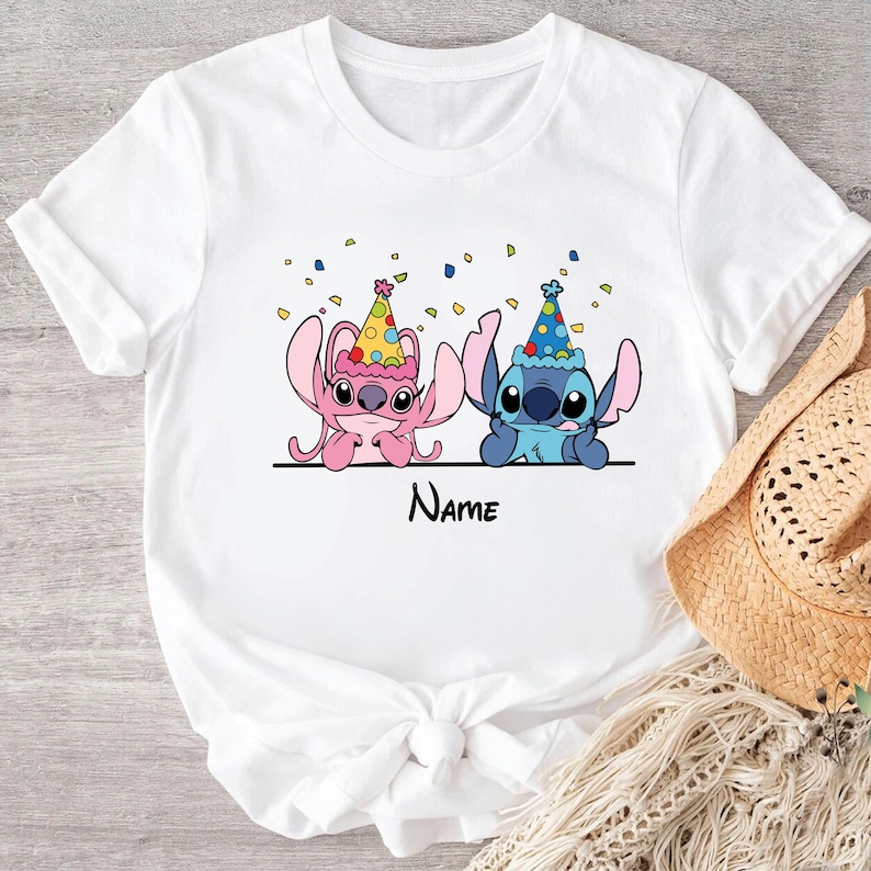 May include: White t-shirt with a pink and blue Stitch character wearing party hats. Confetti is scattered around the characters. The text "Name" is printed below the characters.