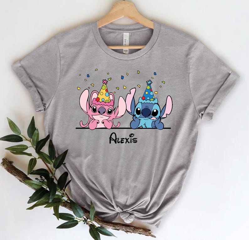 May include: Gray t-shirt with a cartoon image of Stitch and Angel from Lilo & Stitch wearing party hats. The text "Alexis" is printed below the characters.