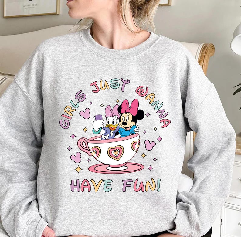 Pu&ograve; includere: Felpa grigia con una grafica di Minnie Mouse e Daisy Duck in una tazza da t&egrave;. Il testo "Girls Just Wanna Have Fun!" &egrave; stampato in colori arcobaleno.
