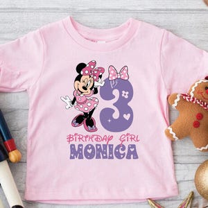 Może przedstawiać: R&oacute;żowa koszulka z kresk&oacute;wkową postacią Minnie Mouse w czerwono-białej sukiencce w kropki. Liczba 3 jest w kolorze fioletowym z r&oacute;żowymi sercami i gwiazdami. Pod obrazkiem znajduje się napis "Birthday Girl Monica".