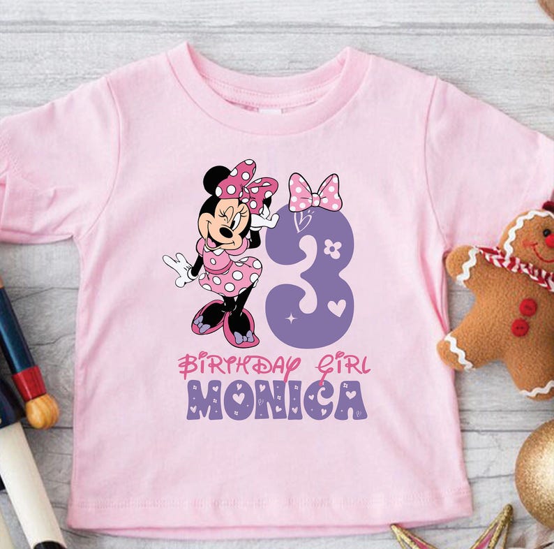 Może przedstawiać: R&oacute;żowa koszulka z kresk&oacute;wkową postacią Minnie Mouse w czerwono-białej sukiencce w kropki. Liczba 3 jest w kolorze fioletowym z r&oacute;żowymi sercami i gwiazdami. Pod obrazkiem znajduje się napis "Birthday Girl Monica".