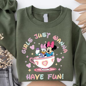 Pu&ograve; includere: Felpa verde con una grafica di due personaggi Disney, Daisy Duck e Minnie Mouse, sedute in una tazza da t&egrave;. Il testo "Girls Just Wanna Have Fun!" &egrave; stampato sulla felpa.