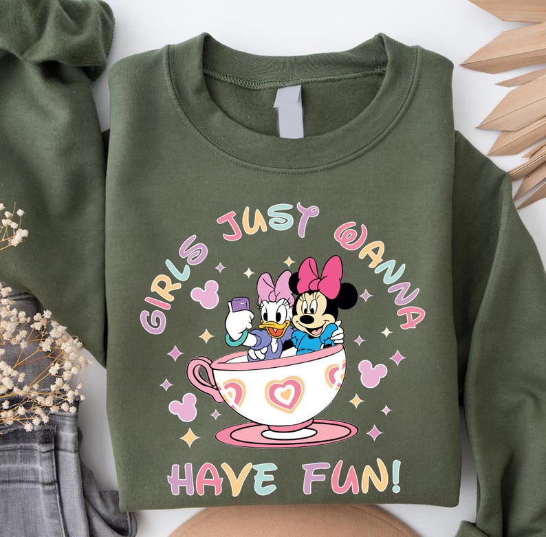 Pu&ograve; includere: Felpa verde con una grafica di due personaggi Disney, Daisy Duck e Minnie Mouse, sedute in una tazza da t&egrave;. Il testo "Girls Just Wanna Have Fun!" &egrave; stampato sulla felpa.