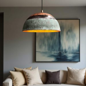 May include: A dome-shaped pendant light fixture with a weathered, textured finish. The top section is dark brown, transitioning to a green-blue hue, with a warm gold interior. The light hangs from a black cord, illuminating a living room setting.