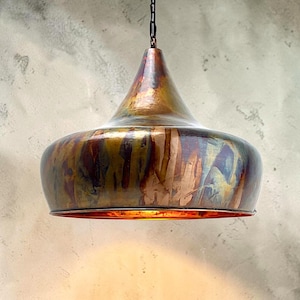 May include: A bell-shaped pendant light fixture with a metallic finish featuring a blend of copper, bronze, and dark iridescent tones. The lamp has a wide, rounded body that tapers toward the top, suspended by a dark metal chain link.