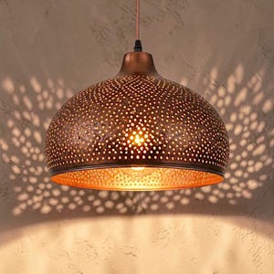 May include: A dome-shaped pendant light fixture with a metallic copper finish, featuring a dense pattern of small circular perforations that allow light to pass through, creating a complex, scattered shadow effect on the surrounding surface.