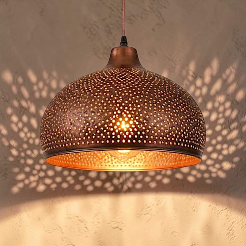 May include: A dome-shaped pendant light fixture with a metallic copper finish, featuring a dense pattern of small circular perforations that allow light to pass through, creating a complex, scattered shadow effect on the surrounding surface.