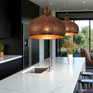 May include: Two dome-shaped pendant lights with a dark bronze exterior finish and intricate laser-cut perforations. The interior of the lamps features a warm, reflective gold-toned surface that glows when illuminated, suspended by thin cords.