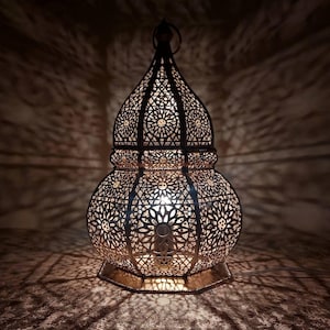 Peut inclure: Une grande lanterne en métal au design complexe avec un sommet en forme de dôme et une base ronde. La lanterne est faite d'un motif délicat et ajouré et est éclairée de l'intérieur, projetant des ombres complexes.