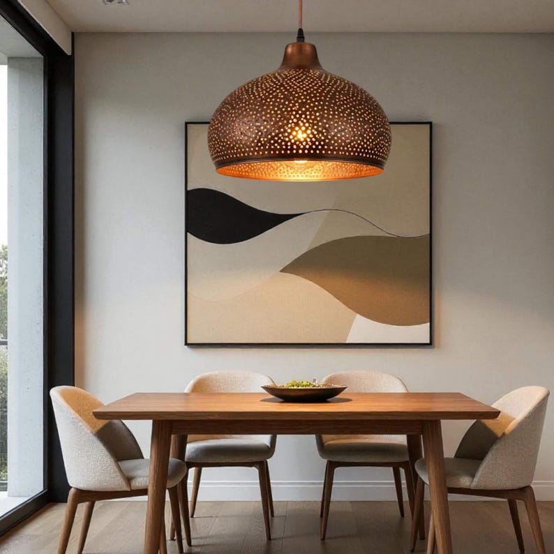 May include: A dome-shaped pendant light fixture with a metallic bronze exterior featuring a perforated pattern that allows light to shine through. The interior of the shade has a warm, reflective gold finish, casting a soft glow downward.
