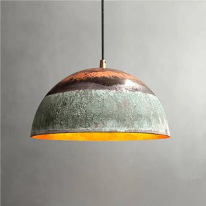 May include: A hanging pendant light with a half-dome shade. The shade features bands of color: orange at the top, a dark brown stripe, and a textured green lower section. The interior glows with a warm, golden light.
