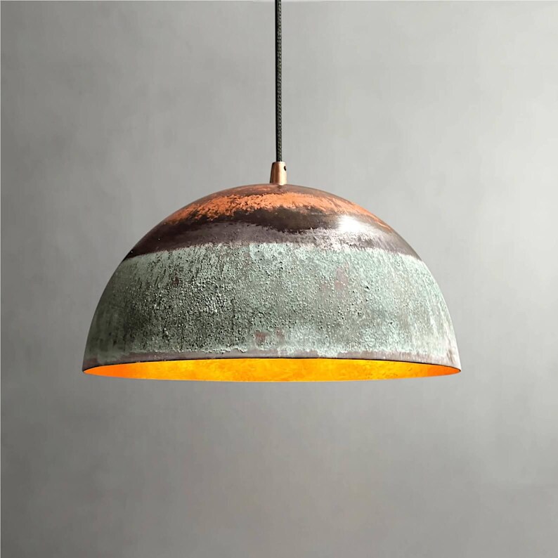 May include: A hanging pendant light with a half-dome shade. The shade features bands of color: orange at the top, a dark brown stripe, and a textured green lower section. The interior glows with a warm, golden light.