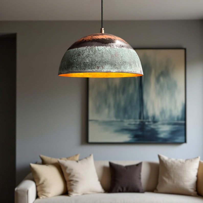 May include: A dome-shaped pendant light fixture with a weathered, textured finish. The top section is dark brown, transitioning to a green-blue hue, with a warm gold interior. The light hangs from a black cord, illuminating a living room setting.