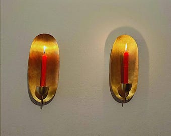 May include: Two gold wall sconces with a red candle in each. The candles are lit and the flames are visible.