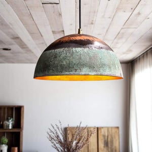 May include: A dome-shaped pendant light fixture with a textured, multi-toned finish. The top section is dark brown, transitioning to a green-blue midsection, and a bright orange interior. It hangs from a black cord with a brass fitting.