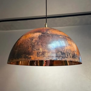 May include: A pendant light with a domed shade, featuring a distressed finish in shades of brown, orange, and black. The interior of the shade has a copper finish. It hangs from a black cord and a brass-toned fitting, creating a vintage aesthetic.