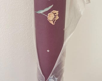 May include: A roll of burgundy wallpaper with a floral pattern. The design features a gold flower with green leaves and small white diamond and flower accents. The wallpaper is partially wrapped in clear plastic.