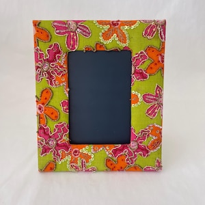 Könnte beinhalten: Ein rechteckiger Fotorahmen mit einem limettengrünen Stoffhintergrund. Der Rahmen ist mit gestickten rosa und orangefarbenen Blumen und Pailletten verziert. Die Fotoöffnung ist dunkelmarineblau.