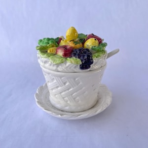 May include: A white ceramic mug with a colourful floral design featuring pink, yellow, and blue flowers. The mug has a curved handle and a glossy finish. The design wraps around the mug.